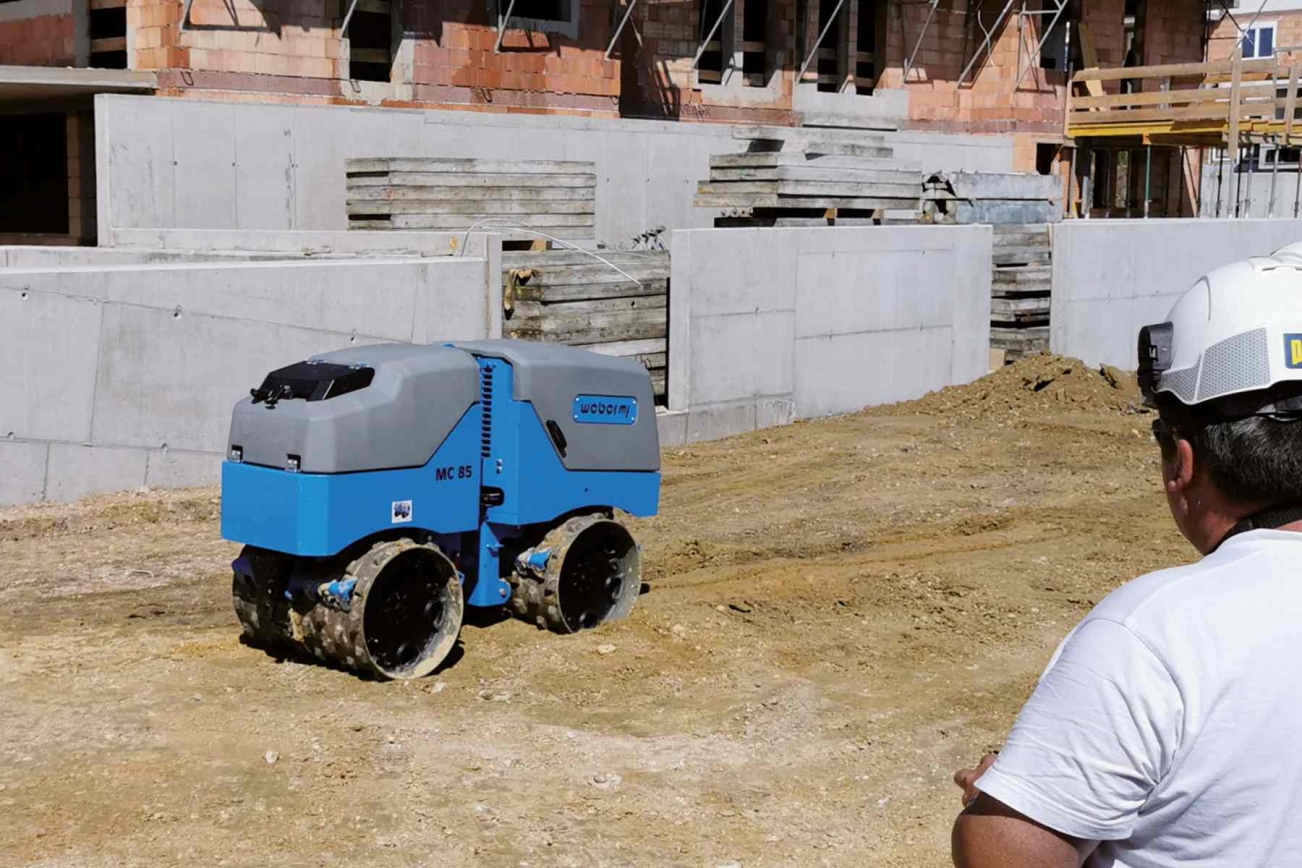 Mann steuert via Fernbedienung blaue Grabenwalze auf Baustelle