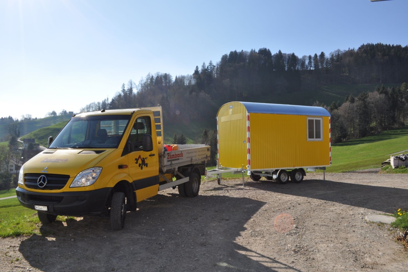 PKW mit orangem RUBAG Baustellenwagen angehängt bei Wald